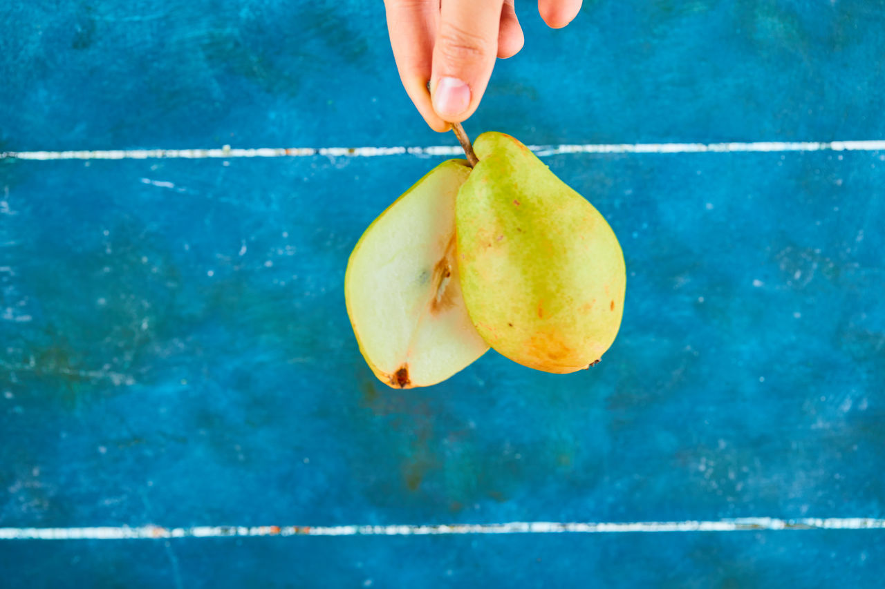 CLOSE-UP OF HAND HOLDING APPLE AGAINST BLUE BACKGROUND