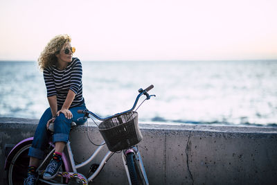 Woman with bicycle on beach against sky