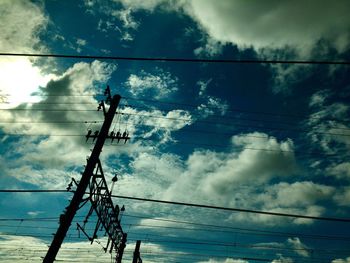 Low angle view of electricity pylon against cloudy sky