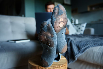 Man with leaky socks resting on sofa, using laptop