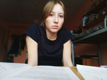 Portrait of young woman by table with books at home