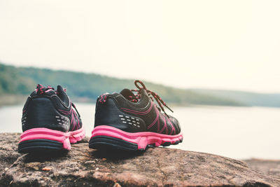 Black shoes on rock by lake against sky