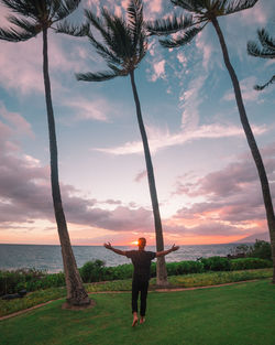 Rear view of man standing by palm tree against sky during sunset