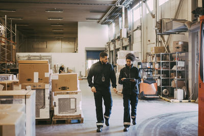 Female and male colleagues discussing over digital tablet while walking in warehouse