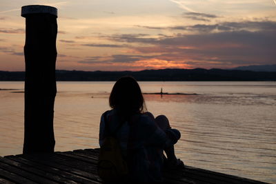 Rear view of woman against sea during sunset