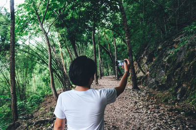 Rear view of man taking selfie while standing on footpath in forest