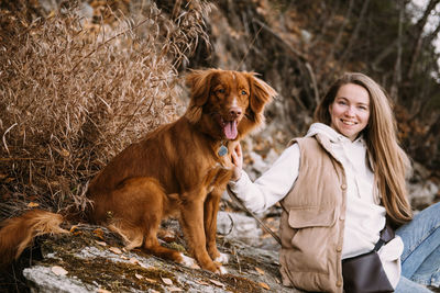 Young woman and dog retriever walks on river shore at autumn season