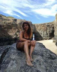 Portrait of woman sitting on rock against sky