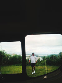 Rear view of man on field against sky seen through window