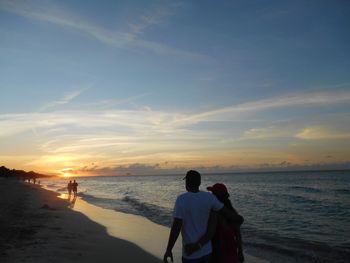Rear view of people on beach against sky during sunset