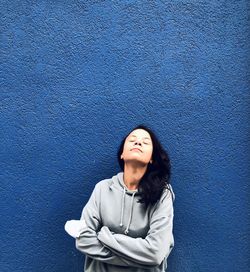 Portrait of smiling young woman standing against blue wall