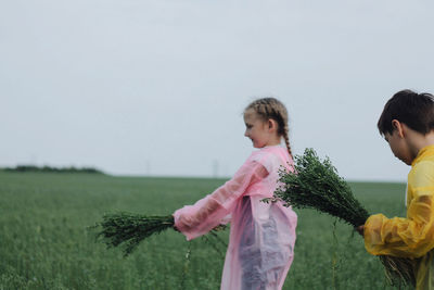 Siblings holding plants on field