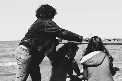 Side view of woman gesturing peace sign by female friends head at shore