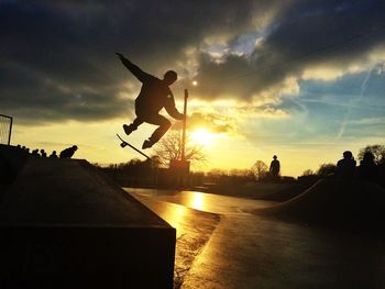 Silhouette man skateboarding at skateboard park against sky at sunset