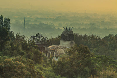 Built structure by trees against sky during sunset