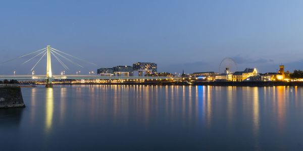 Illuminated city by sea against clear sky at night