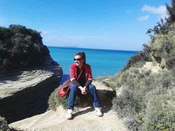 Full length of young woman sitting on beach against sky