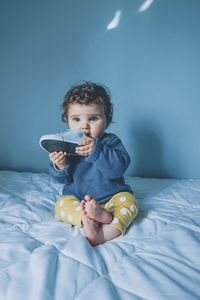 Cute girl holding shoe while sitting on bed