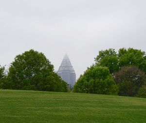 Trees growing by building against sky at park