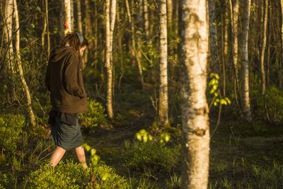 Side view of woman walking on field amidst trees at forest