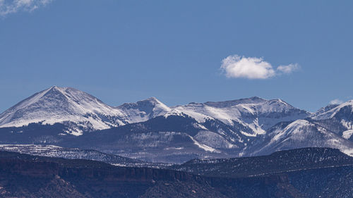 Panoramic scenic view of snow capped mountains with blue sky and a puffy white cloud