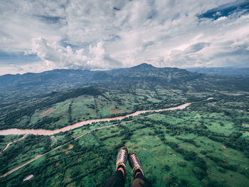 Low section of person on mountain against cloudy sky