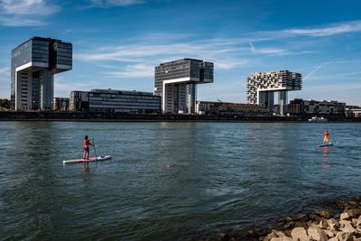 People on sea by city against sky