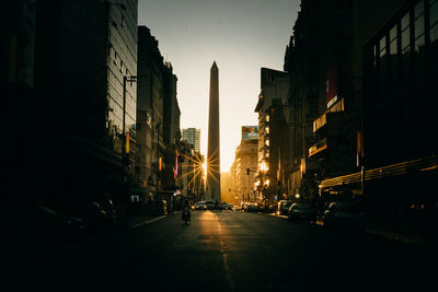 City street amidst buildings against sky during sunset