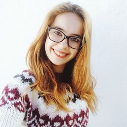 Portrait of smiling young woman wearing eyeglasses against wall