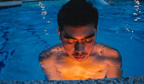 Close-up of young man in illuminated swimming pool at dusk