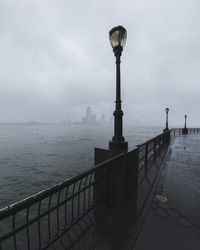 Street lights on promenade by river during foggy weather