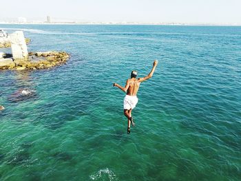 Rear view of man jumping in sea against clear sky