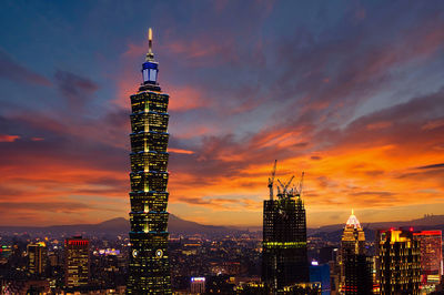 Illuminated buildings in city against sky during sunset