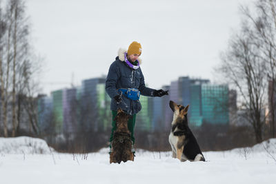 Man playing with dogs on snow covered land against sky