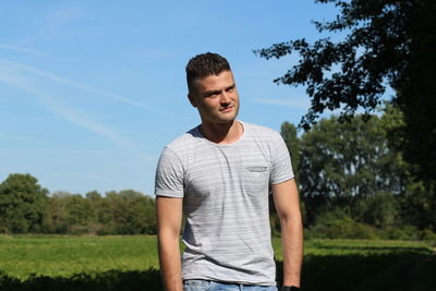 Smiling young man standing by trees against sky