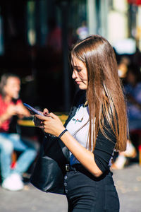 Side view of young woman using mobile phone outdoors