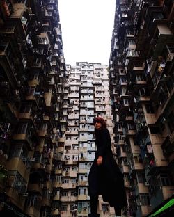 Side view of woman walking amidst buildings in city against sky