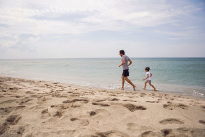 Father in a striped t-shirt walks with his son in shorts and a t-shirt walking on the beach