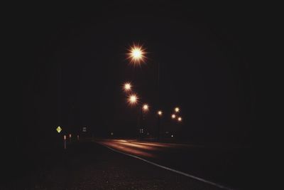 Illuminated road against sky at night