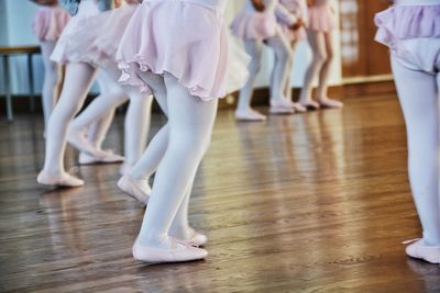 Low section of girls performing ballet on hardwood floor