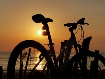 Silhouette bicycle by sea against sky during sunrise