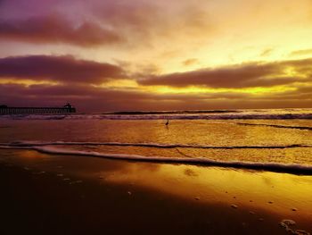 Scenic view of beach against dramatic sky during sunset