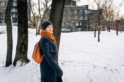 A woman in winter clothes with a leather red backpack looks around smiling