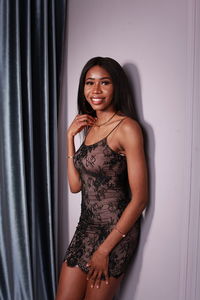 Cropped front side portrait of african woman in short party dress leaning on wall in studio