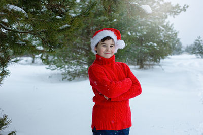 Cute teenager in a red sweater and a red santa claus hat stands in the winter in the park