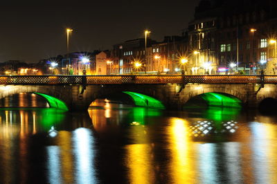 Illuminated bridge over river in city at night