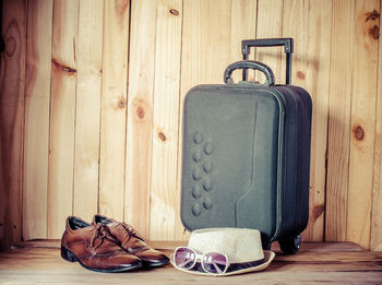 Leather shoes by hat and sunglasses with luggage against wooden wall