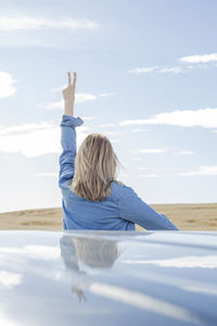 Rear view of woman gesturing peace sign against sky