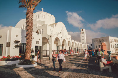 People walking by orthodox metropolitan cathedral against sky on sunny day