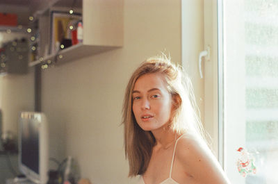 A woman stands in front of a window in an apartment